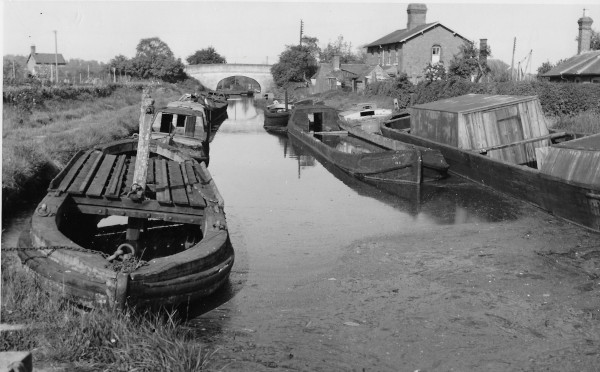 image Graveyard of Boats! Scene on the Shropshire Union Canal at Norbury Junction (Shropshire Union main line & Shrewsbury Canal) derelict? boats parked in abandoned Shrewsbury Canal above top lock (now converted into a dry dock) April 1955. Icebreaker=Brewood